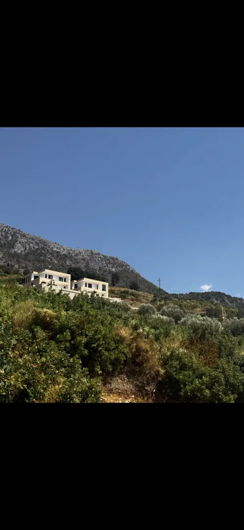 Pogled na kuće okružene zelenilom i brdima u pozadini.