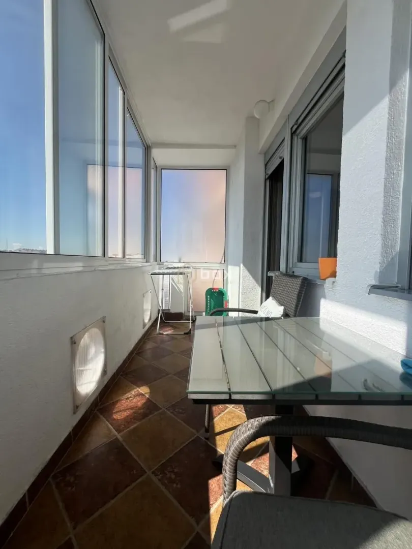Enclosed balcony with a table, chairs, and tiled flooring.