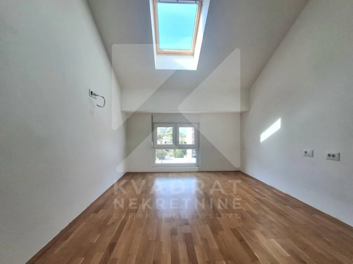 Empty attic room with parquet flooring and a skylight.