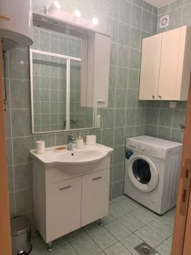 Small tiled bathroom with a sink, mirror, and washing machine. - image 5