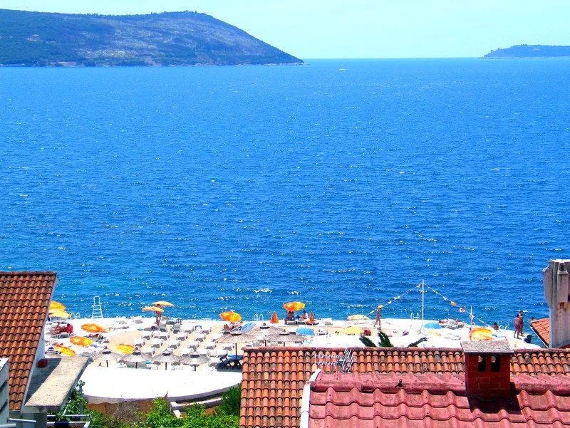 Pogled na more i plažu preko krovova kuća.