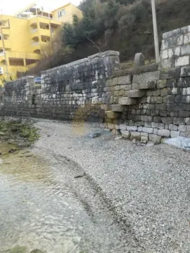 Kameni zid pored obale i plaže sa zgradom u pozadini. - image 3