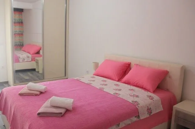 Spavaća soba sa bračnim krevetom, roze posteljinom i ugradnim plakarom sa ogledalom.