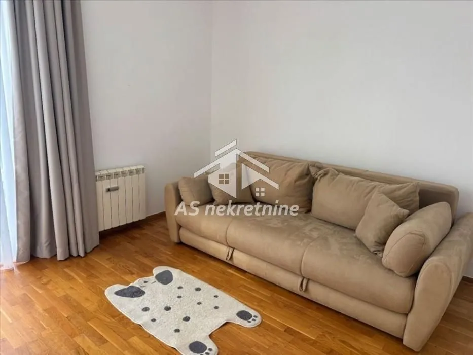 Living room with a beige sofa and hardwood flooring.