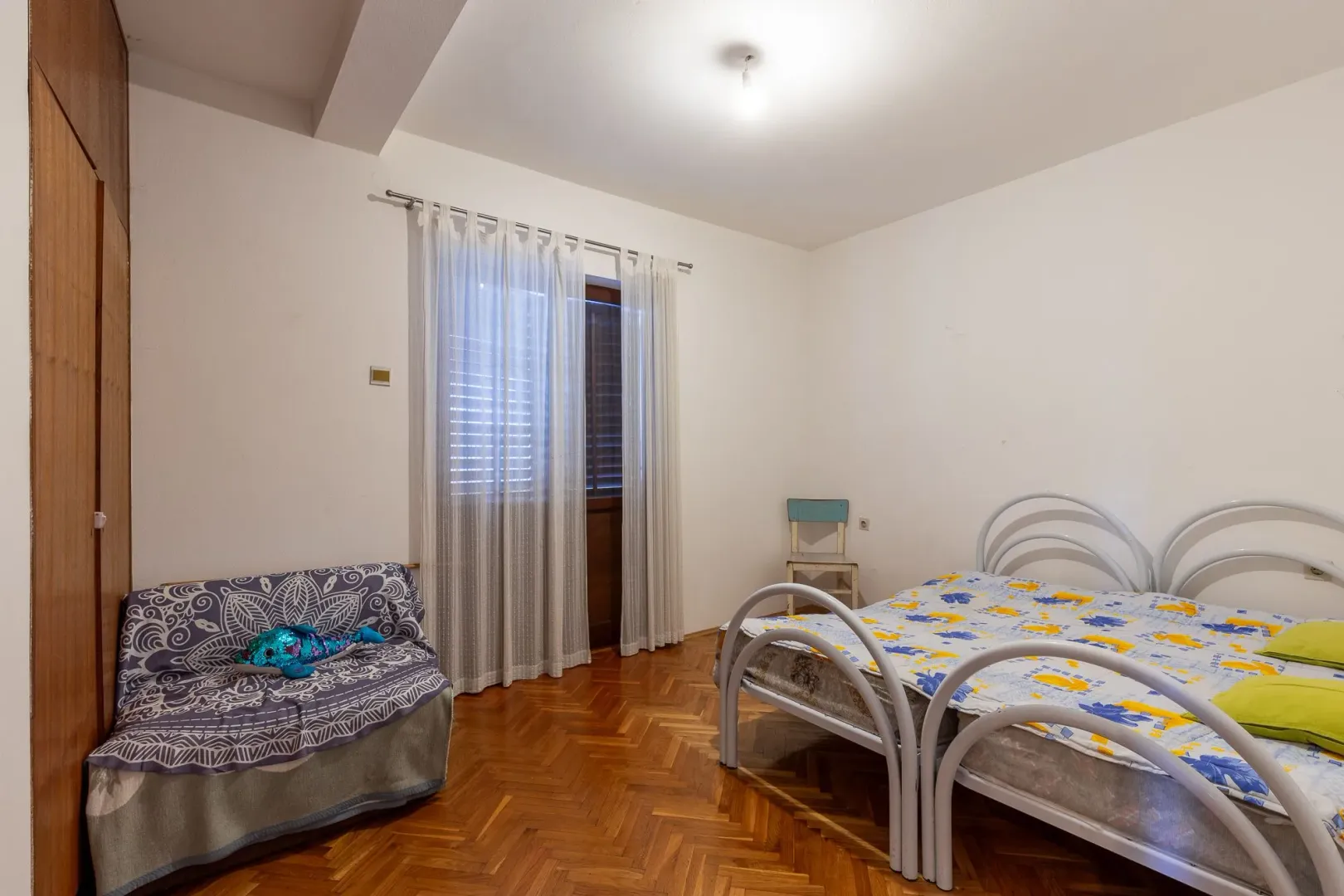 Spavaća soba sa krevetom, trosjedom, parketom i izlazom na balkon.