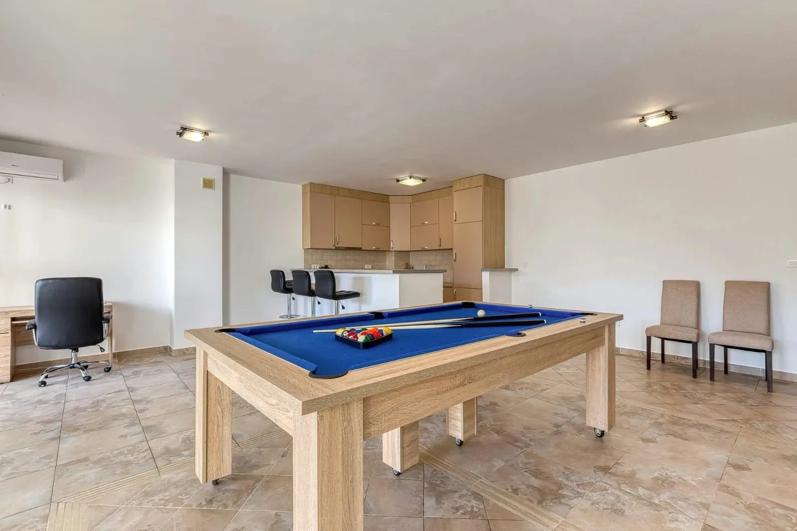 Spacious living room with a pool table and a kitchen in the background.