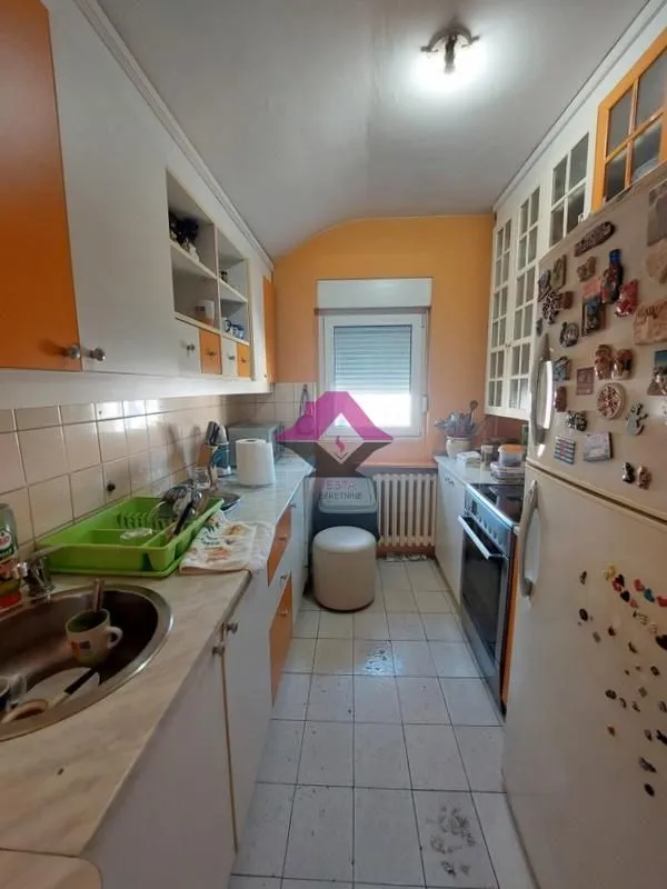 Manja kuhinja sa belim i narandžastim elementima i frižiderom.
