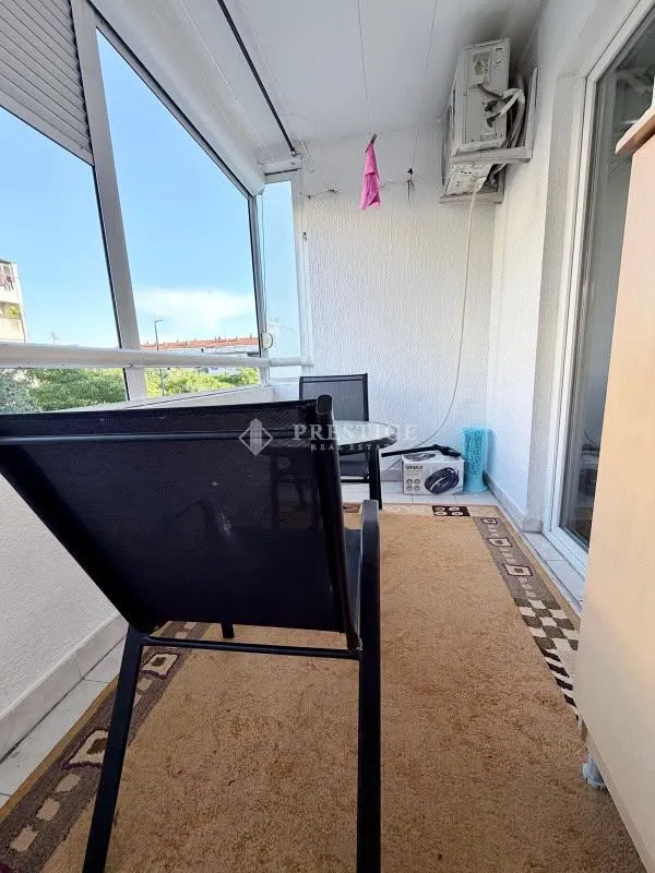 Zastakljeni balkon sa garniturom za sedenje i klimom.