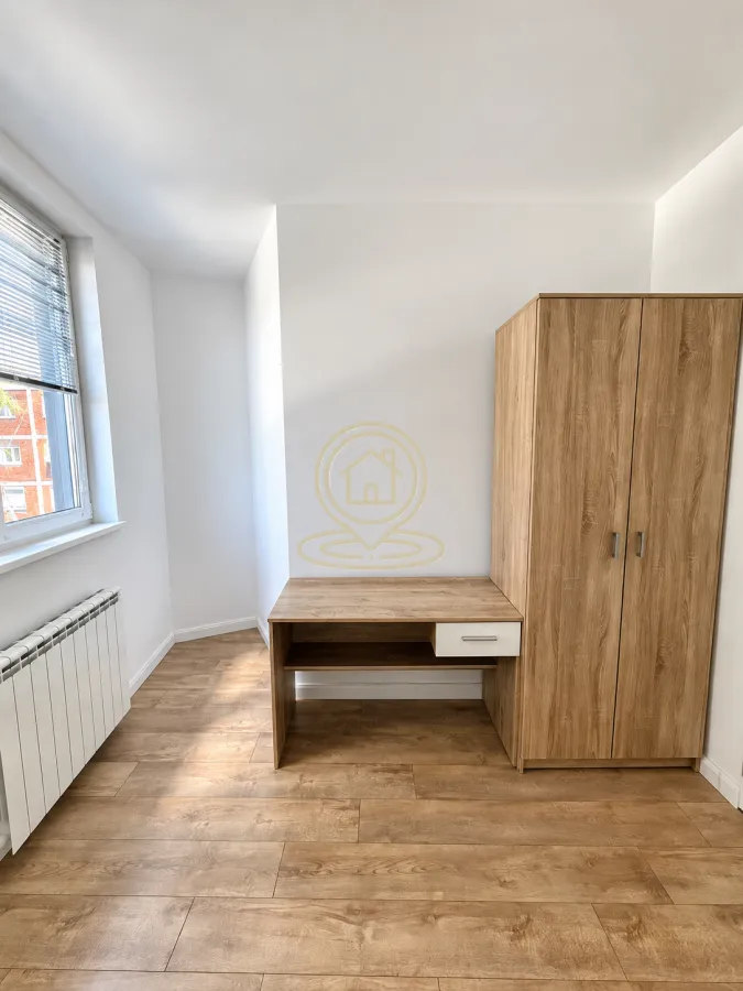 Manja soba sa drvenim garderoberom, radnim stolom i prozorom.