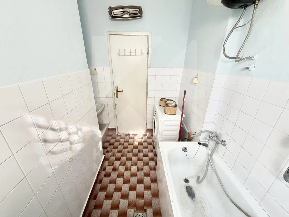 Smaller bathroom with a bathtub, washing machine, and tiled walls and floor.