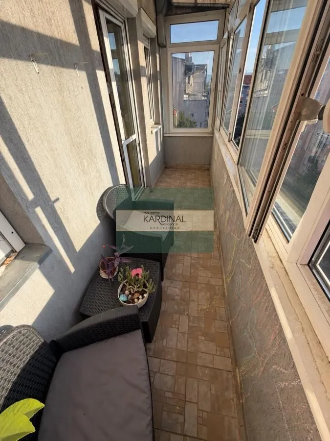 Zastakljeni balkon sa garniturom za sedenje i keramičkim pločicama na podu.
