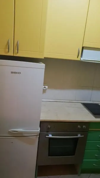 Manja kuhinja sa žutim i zelenim elementima, frižiderom i ugradnom rernom.