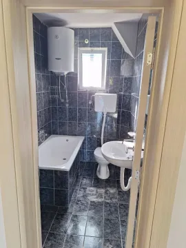 A small bathroom with a bathtub, sink, and water heater, decorated with dark tiles. - image 13