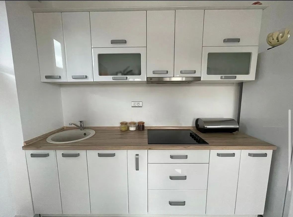 Small white kitchen with a wooden countertop and built-in appliances.