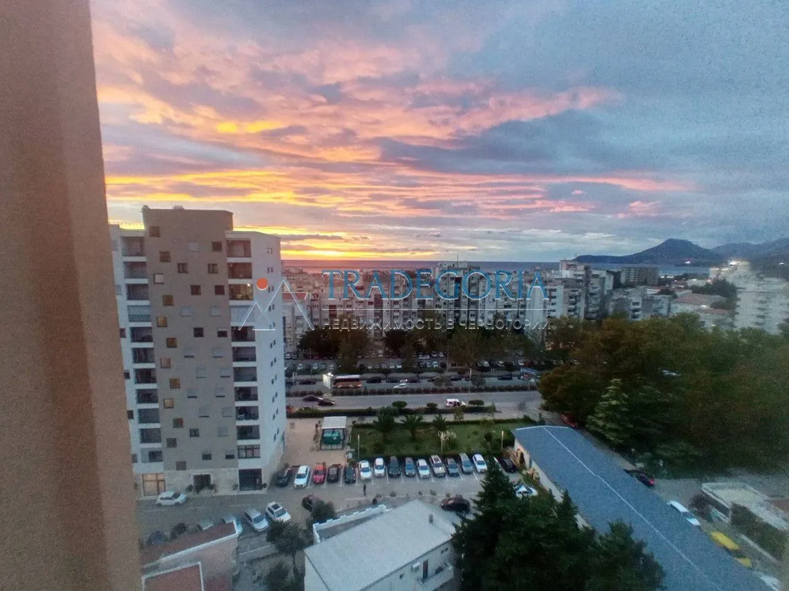 Pogled sa prozora na grad i more tokom zalaska sunca.