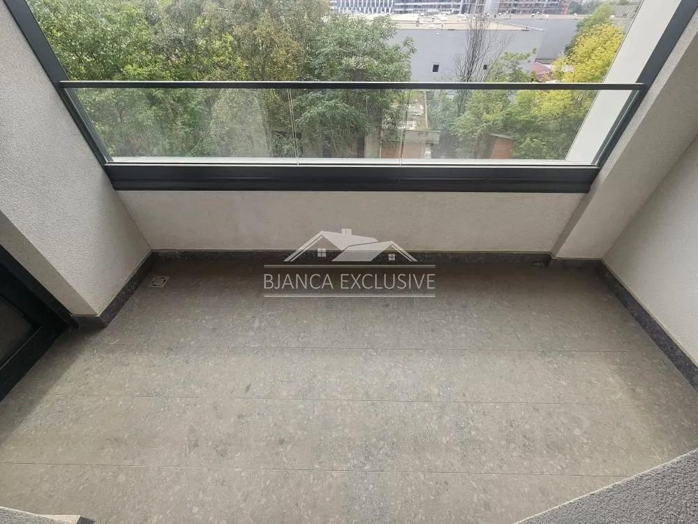 Manji natkriveni balkon sa staklenom ogradom i pogledom na zelenilo.