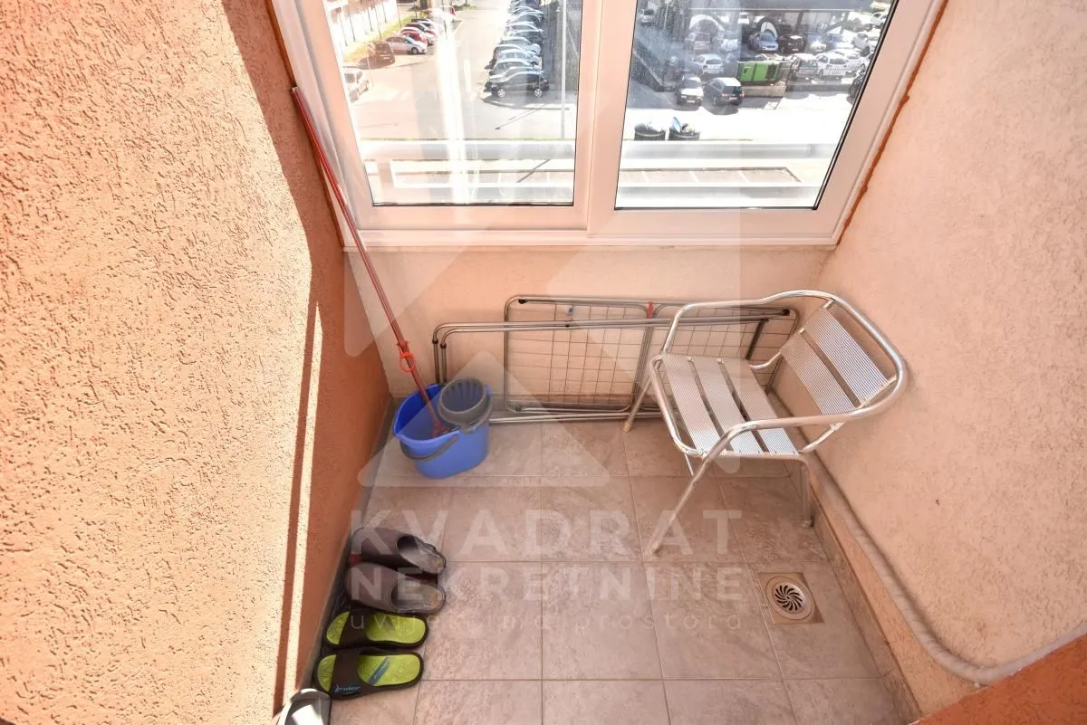 Small tiled balcony with a window and cleaning equipment.