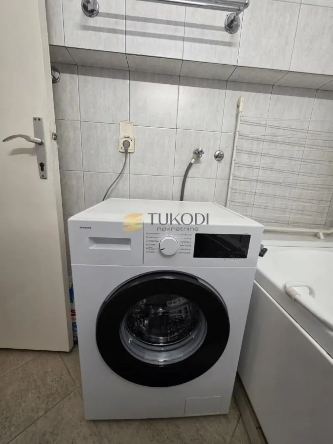 Kupatilo sa veš mašinom i kadom obloženom pločicama.