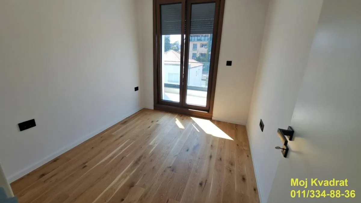 Prazna soba sa drvenim podom i balkonskim vratima.