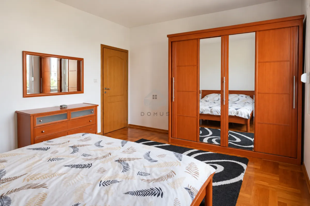 Furnished bedroom with a large double bed, wooden wardrobe, and a dresser with a mirror.