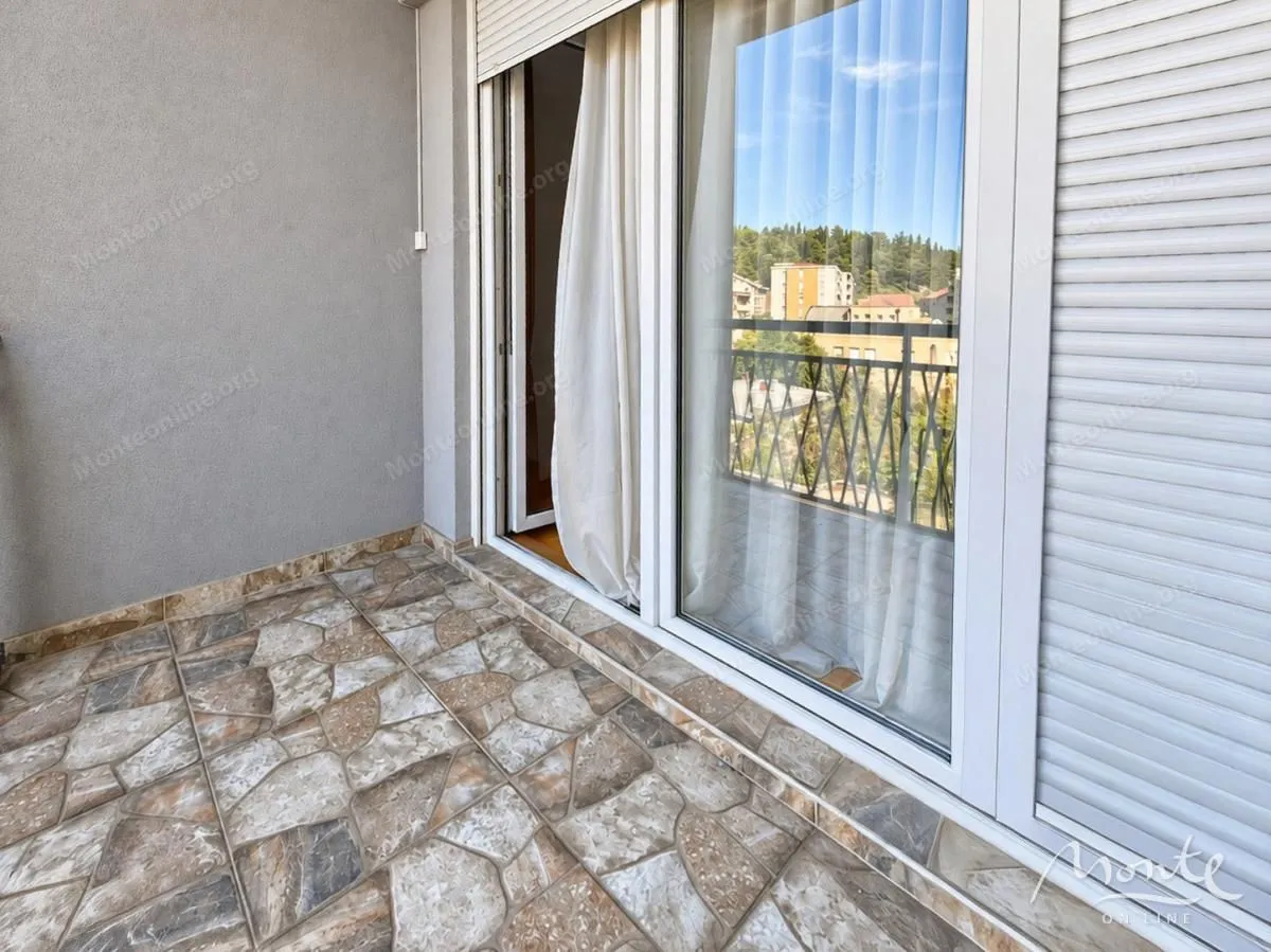Natkriveni balkon sa popločanim podom i pogledom na okolinu.