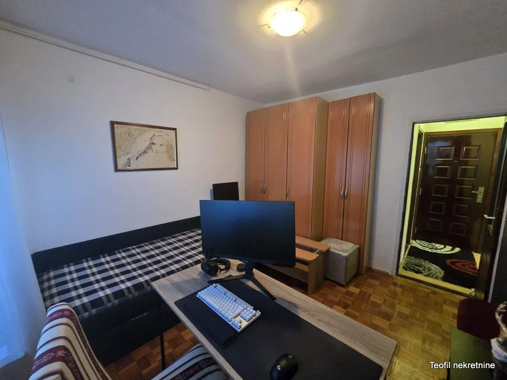 Manja spavaća soba sa krevetom, radnim stolom i garderoberom.