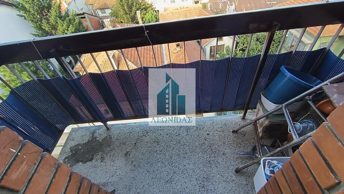 Manji balkon sa zaštitnom ogradom i pogledom na okolne zgrade i krovove.