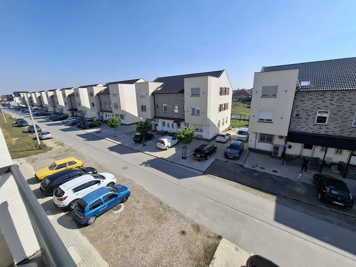 Pogled sa terase na redove modernih zgrada i parkirana vozila u ulici.
