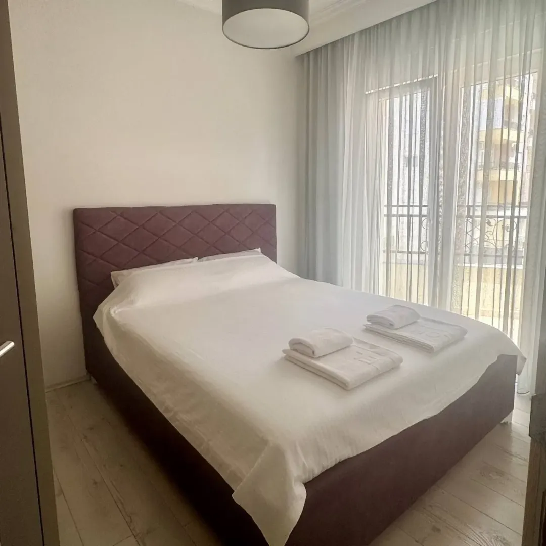 Furnished bedroom with a double bed and a window with light curtains.