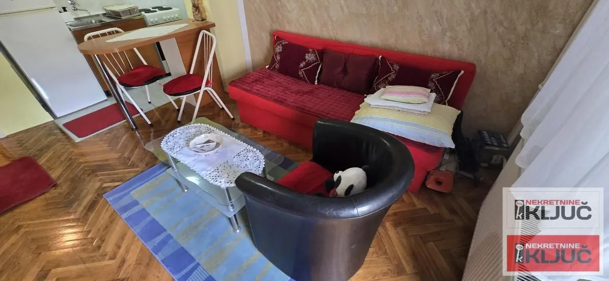 Dnevna soba sa garniturom i malom kuhinjom u pozadini.