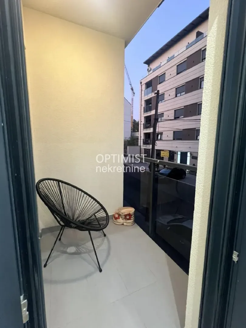 Manji namešten balkon sa staklenom ogradom i stolicom.