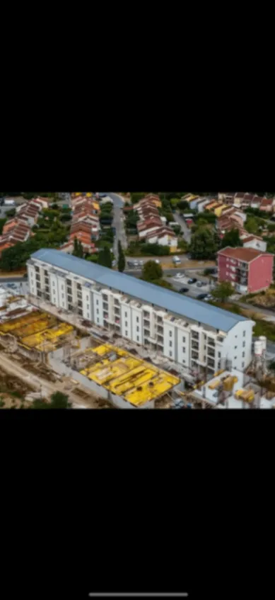 Pogled iz vazduha na stambenu zgradu i okolno naselje.