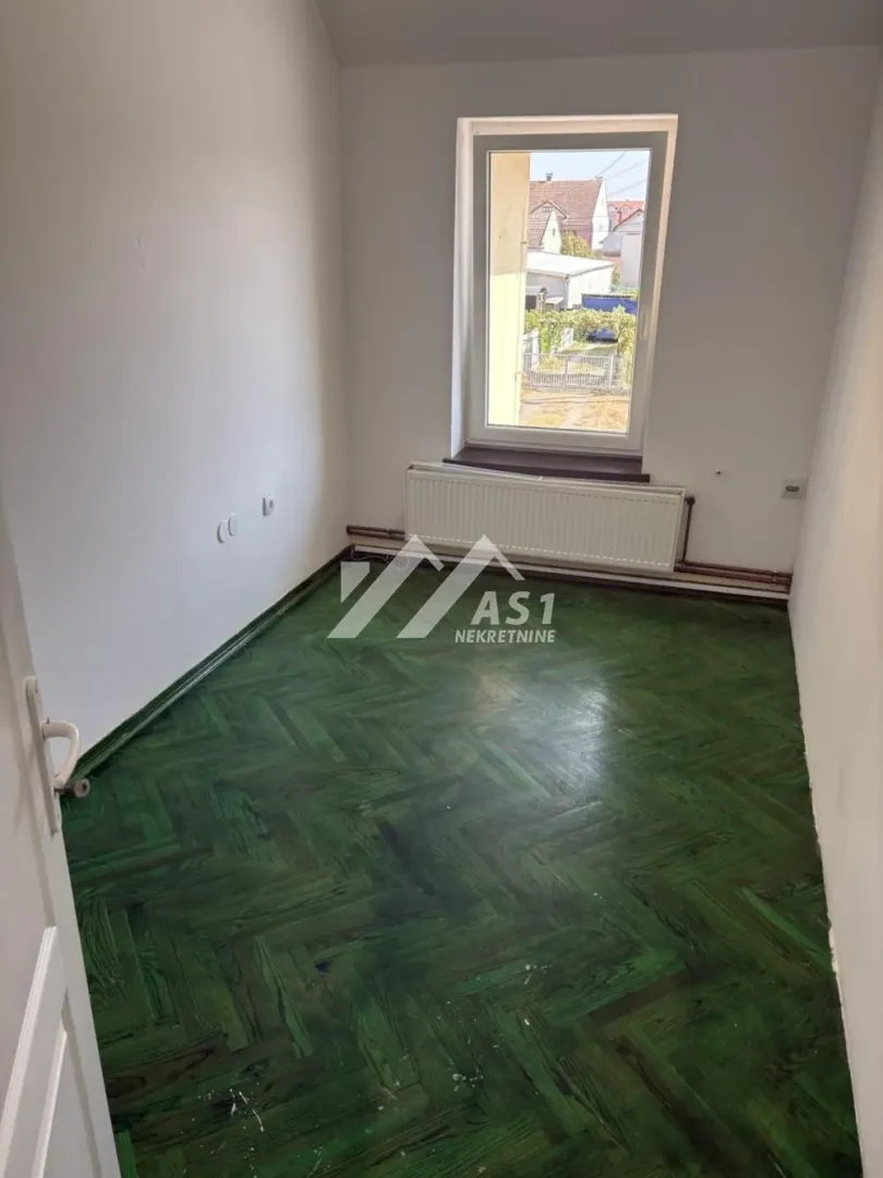 Empty room with green parquet flooring and a single window.