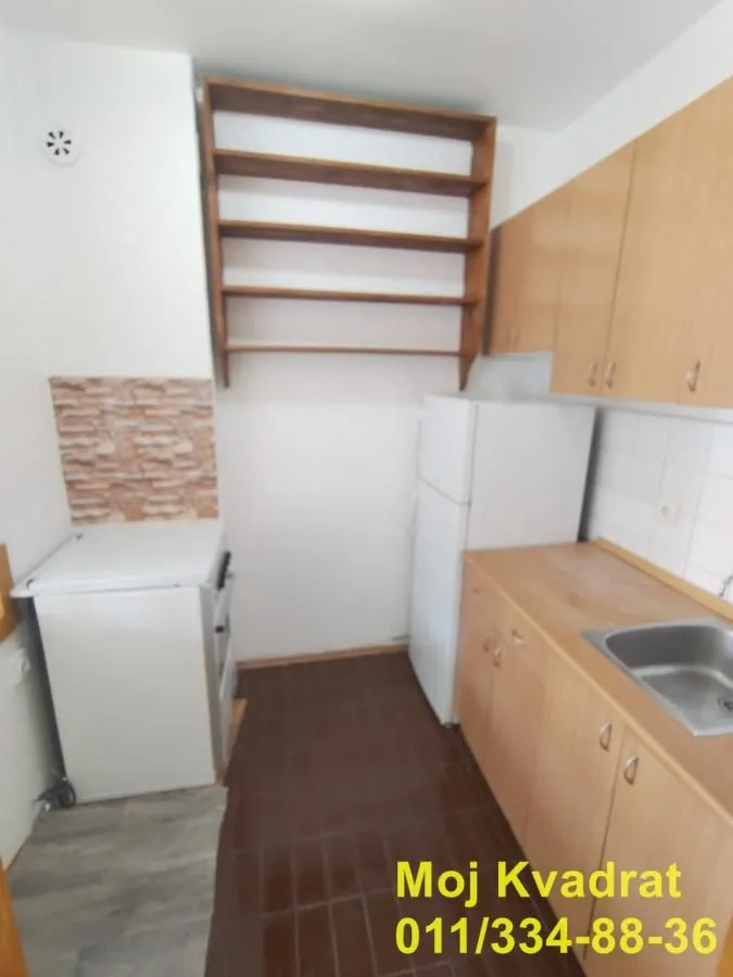 Manja kuhinja sa drvenim elementima, frižiderom i šporetom.