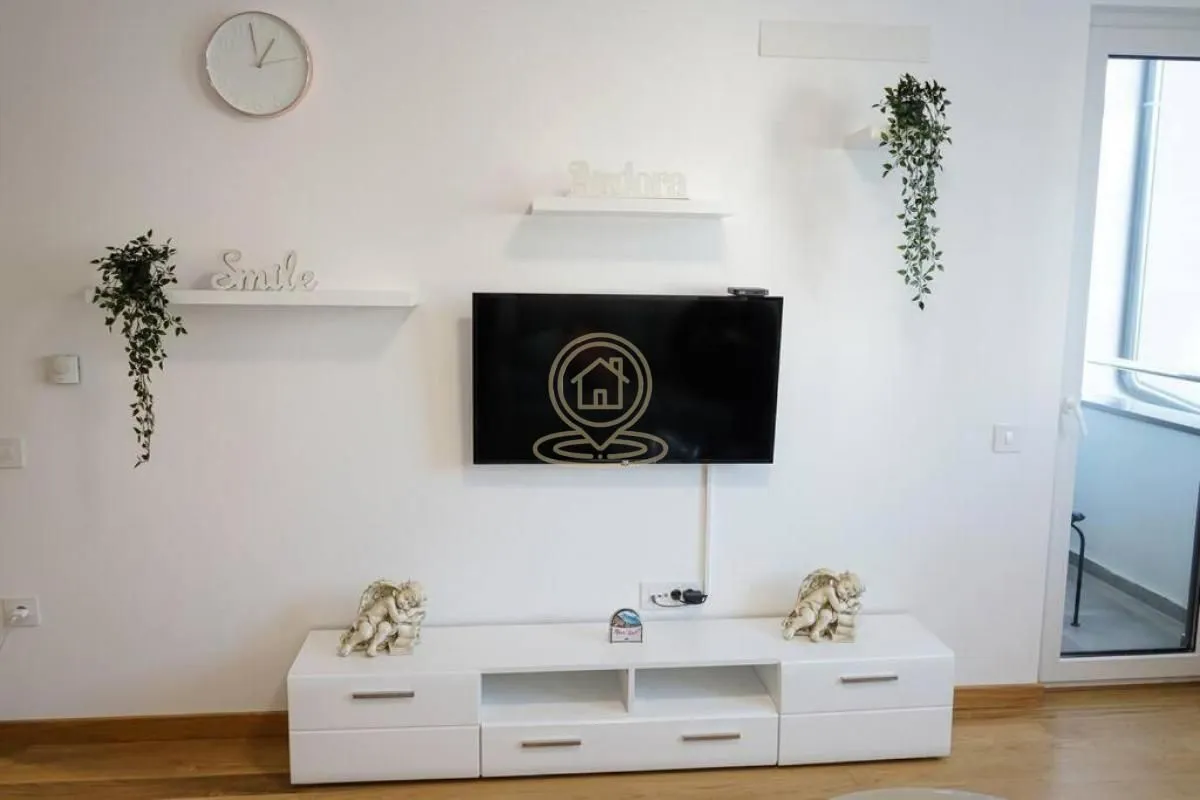 Dnevna soba sa belom komodom, televizorom na zidu i dekorativnim policama.