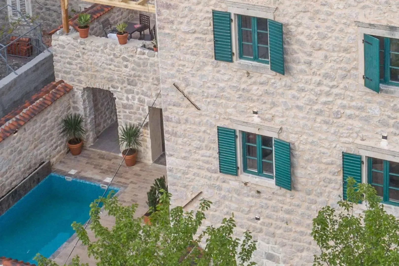 High-angle view of the stone house facade, courtyard with a swimming pool, and terrace.