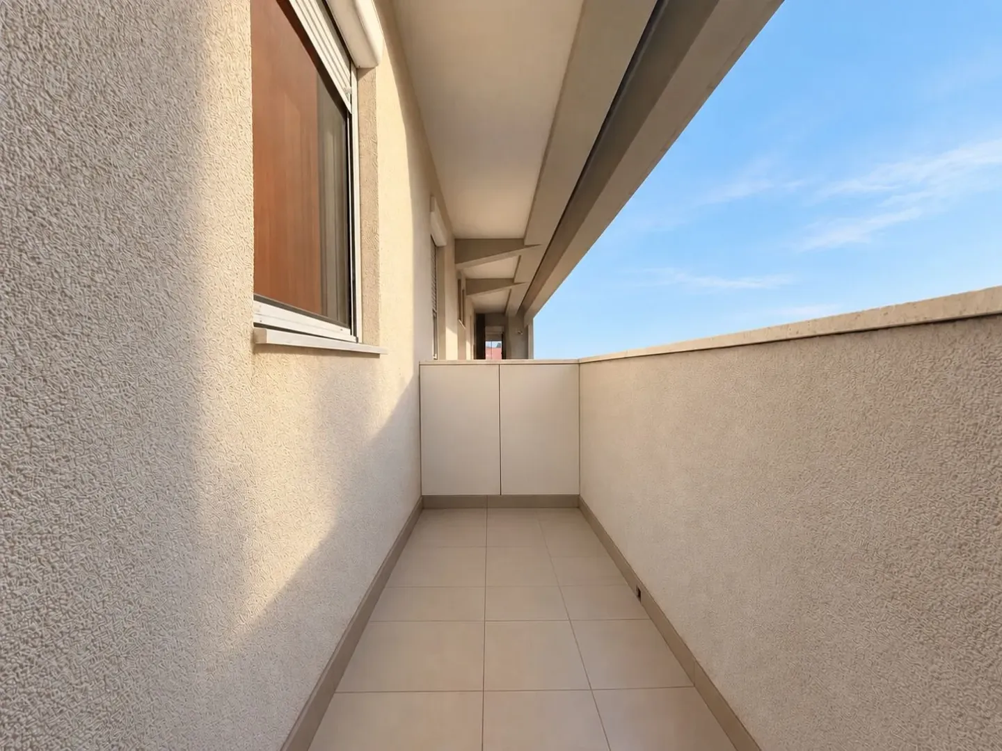 Dugački natkriveni balkon sa pločicama i ugrađenim ormarićem na kraju.