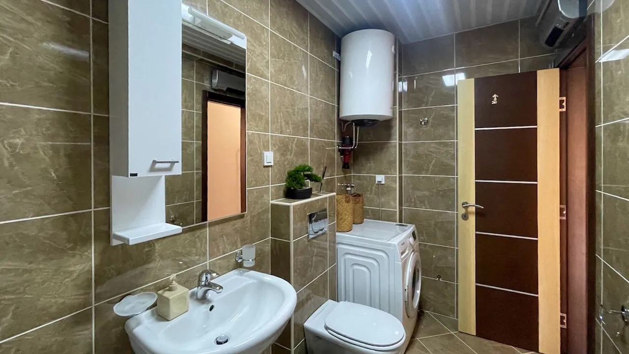 Kupatilo opremljeno sanitarijama, umivaonikom, ogledalom i mašinom za veš.
