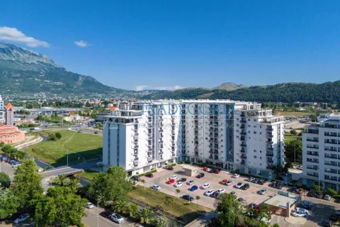 Pogled iz vazduha na stambenu zgradu sa okolnim parkingom i planinama u pozadini. - image 11
