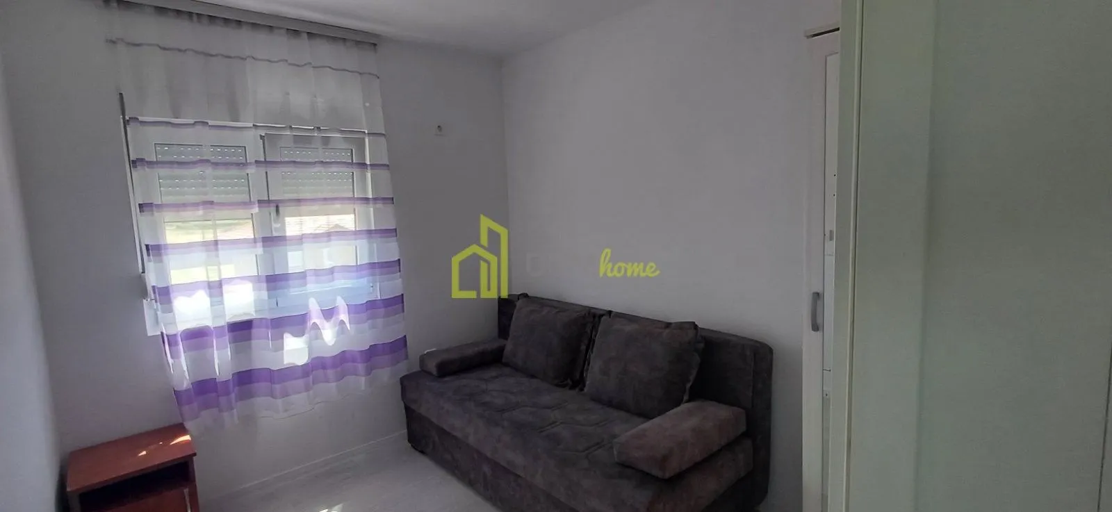 Small living room with a sofa and a window with purple curtains.