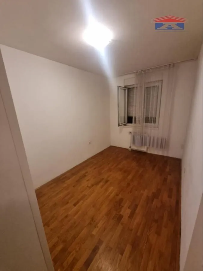 Prazna soba sa parketom i belim zidovima.