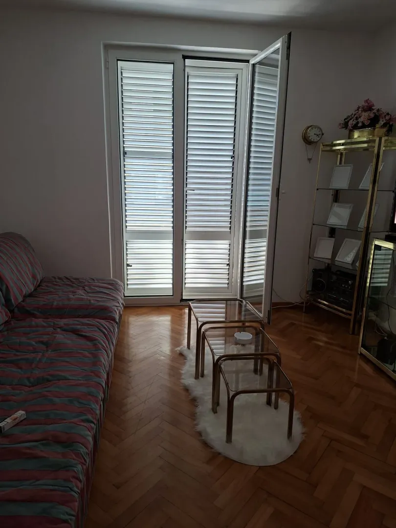 Dnevna soba sa garniturom za sjedenje, staklenim stočićem i balkonskim vratima.