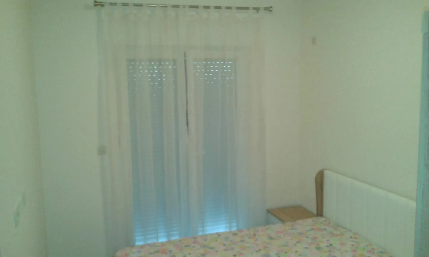 A simple bedroom featuring a bed and balcony doors with curtains.