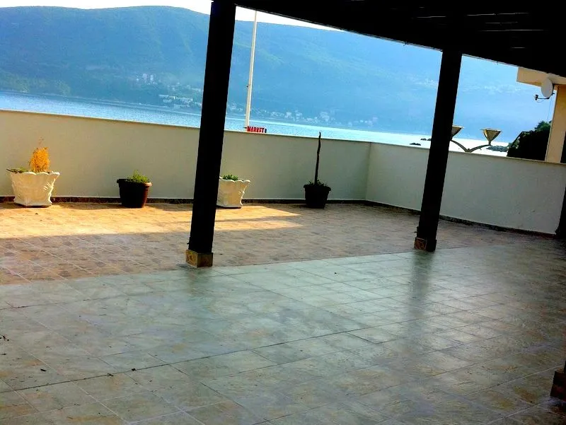Prostrana popločana terasa sa pogledom na more i okolne planine.