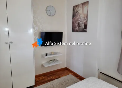 Manja spavaća soba sa krevetom, garderoberom, zidnim televizorom i dekorativnim satom. - image 9