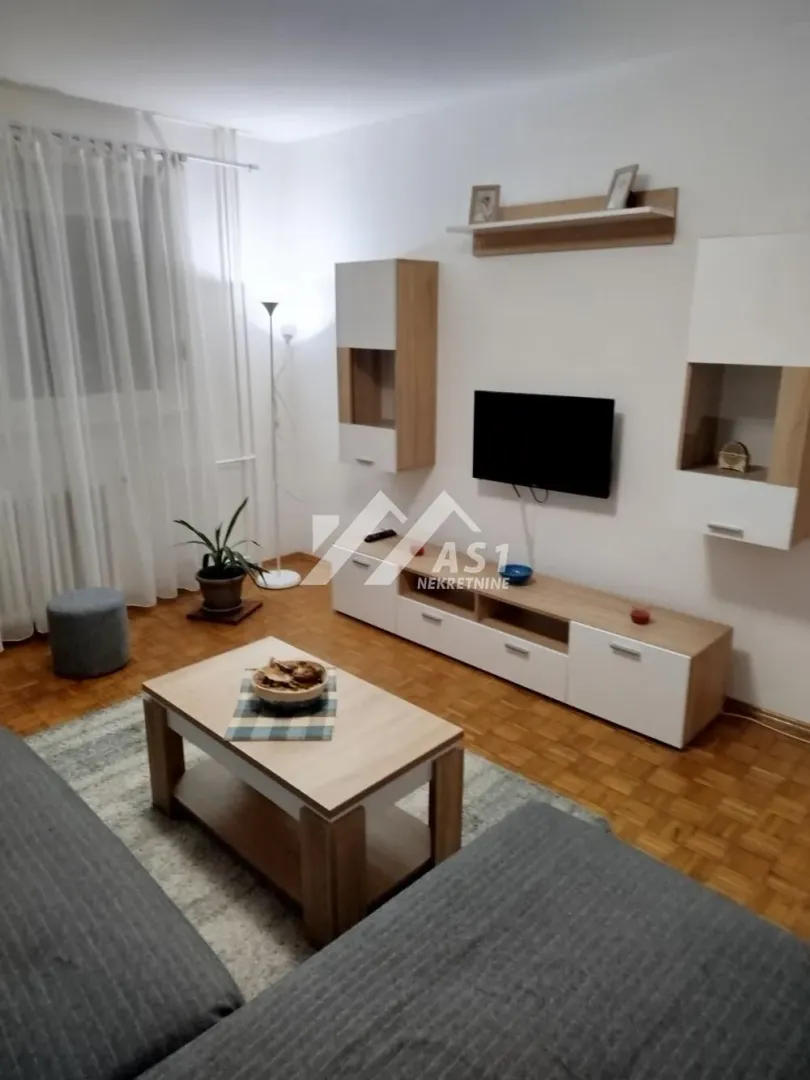 Nameštena dnevna soba sa garniturom, TV-om i drvenim nameštajem.