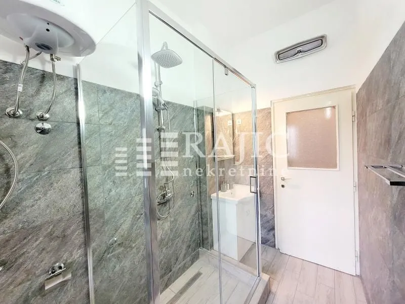 Modern bathroom with a glass shower enclosure and stone-effect tiles.