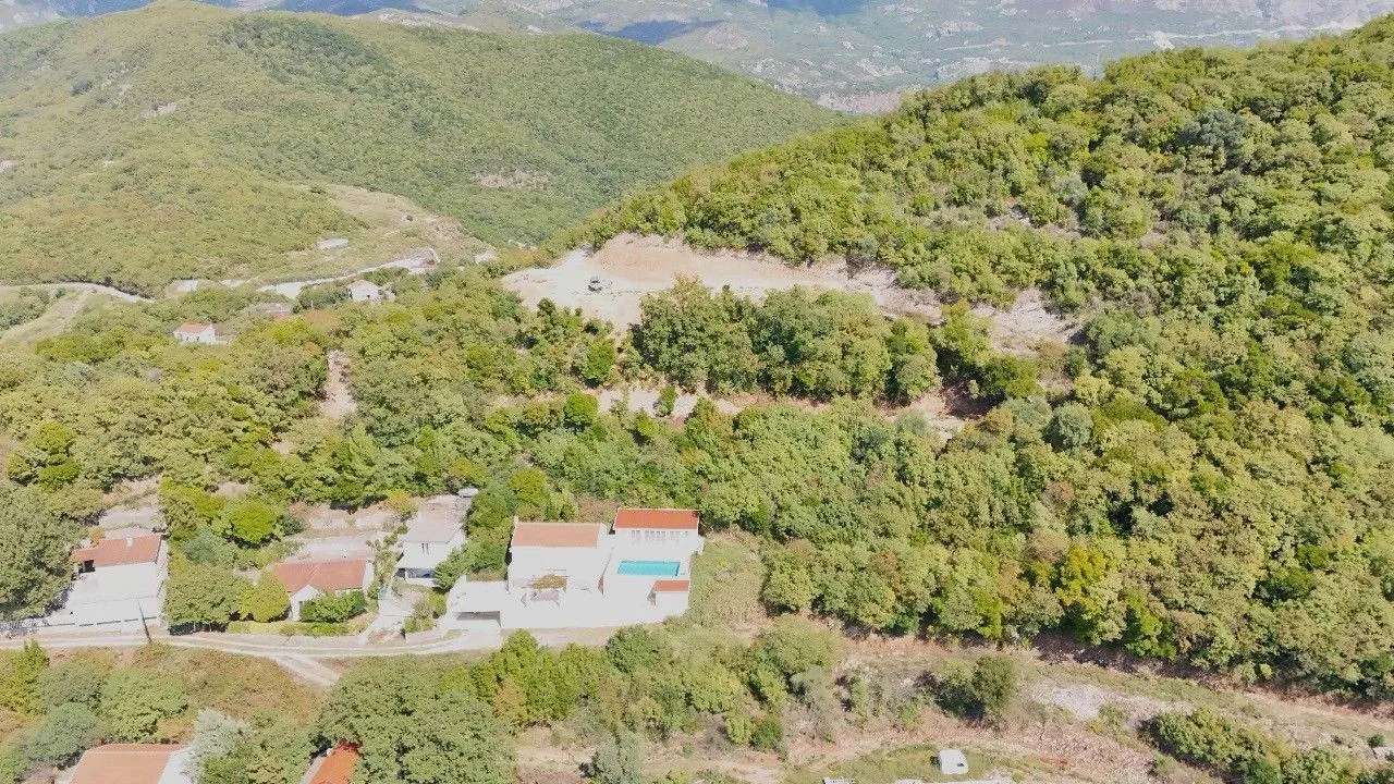 Pogled iz vazduha na imanje sa kućom i bazenom okruženo šumom i brdima.