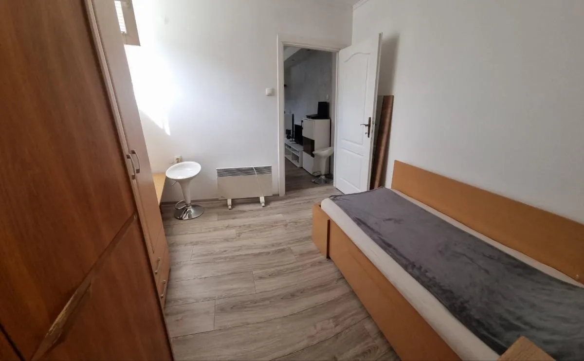 Manja spavaća soba sa krevetom, ormanom i stolom sa stolicom.