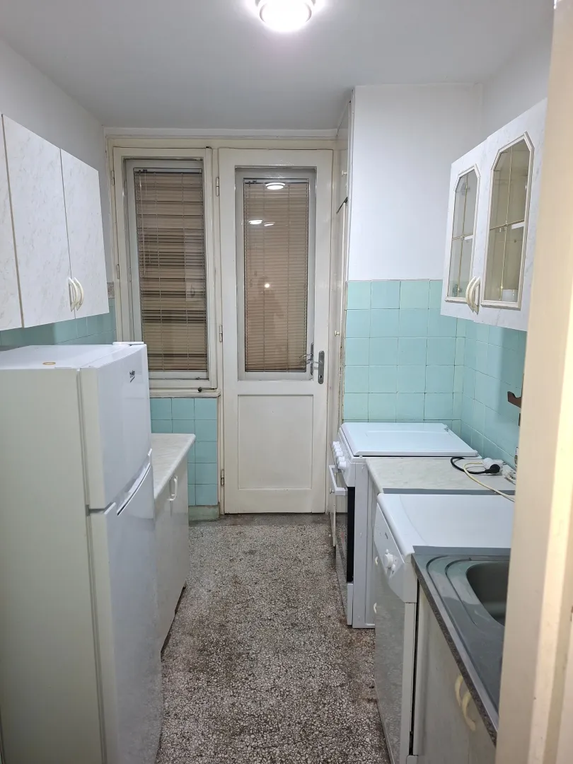Small kitchen with white cabinets, a refrigerator, and a door leading to the terrace.